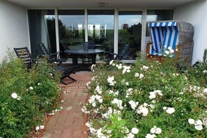 En uteplats med ett bord och stolar, omgiven av vita blommor och en gång av tegelstenar.