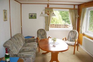 Een kamer met een houten eettafel, twee gestreepte stoelen, een bank, een raam met gordijnen en een fles op een tafel.