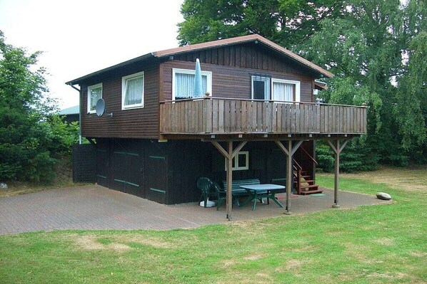 Een houten huis met twee verdiepingen, een balkon, een schotelantenne en een geplaveid pad.