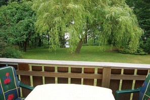 Een terras met uitzicht op een treurwilg en omliggend groen.