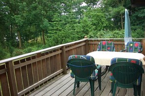 Een houten terras met een tafel en stoelen, omringd door bomen.