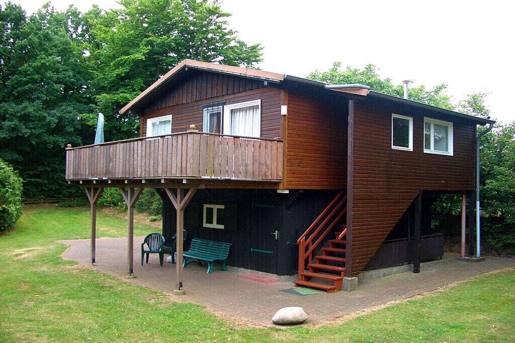 A two-story wooden house with a balcony and a staircase leading to the upper floor.