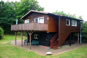 Een houten huis met twee verdiepingen, met een balkon en een trap naar de bovenverdieping.