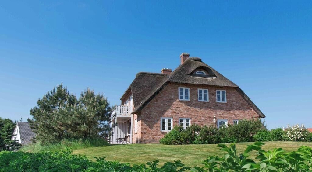 A large brick house with a steeply pitched roof, a visible chimney, and a small porch with a railing.