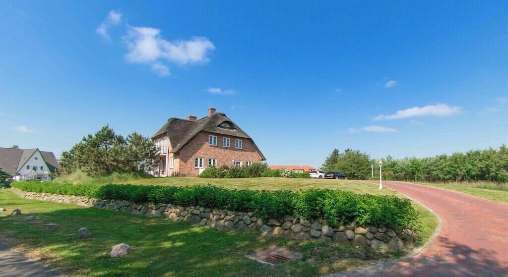 Une grande maison en briques, dotée d’un toit en pente, entourée d’une pelouse bien entretenue et d’un mur de pierres.