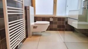 Une salle de bain moderne avec des toilettes, une douche à parois de verre et un radiateur blanc.