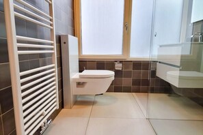 Een moderne badkamer met toilet, een douchecabine van glas en een witte radiator.