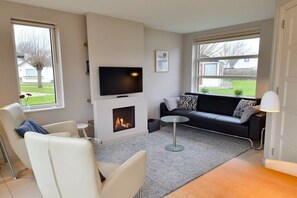 Een moderne woonkamer met een open haard, een bank, een televisie en een eethoek.