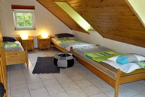 Et soveværelse med to træsenge, et lille vindue og et skråt loft.