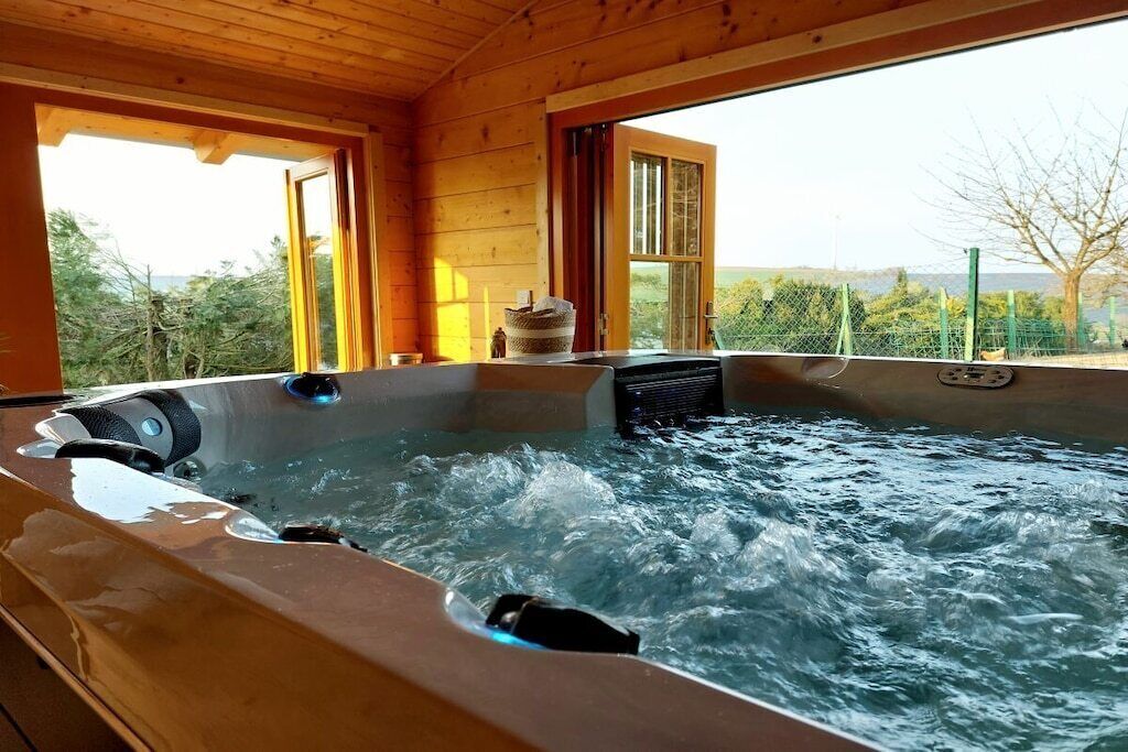 A hot tub in a wooden cabin with a view of the outdoors.
