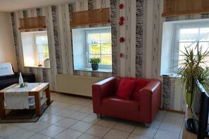 A living room with a red sofa, a coffee table, a TV, and a window with a view of greenery. - Holiday home with 4 bedrooms (Plütscheid)