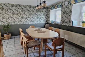 Een eethoek met een ronde tafel, stoelen, een potplant en een muur met een bladmotief.