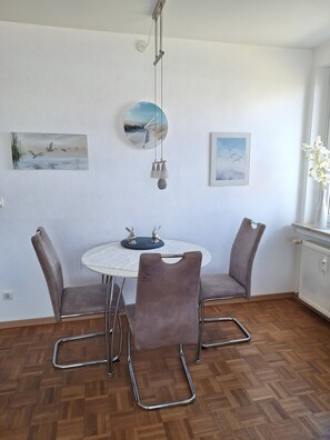 A dining area with a round table, four chairs, and a hanging light fixture. - Bright Holiday Apartment with Balcony Near the Beach (Lübeck)