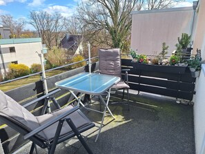 An outdoor balcony with a glass table and two chairs, a black fence, and potted plants. - Bright Holiday Apartment with Balcony Near the Beach (Lübeck)