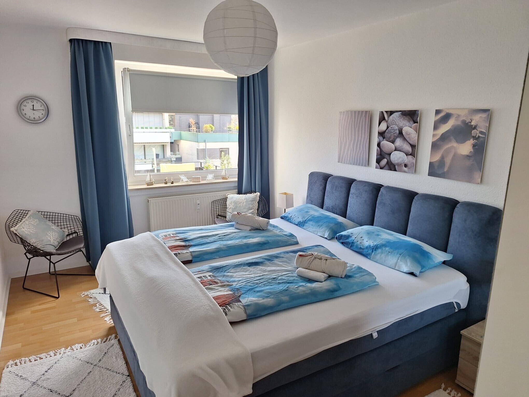 A bedroom with a large bed, a window with curtains, a chair, and artwork on the wall.