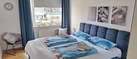 A bedroom with a large bed, a window with curtains, a chair, and artwork on the wall.
