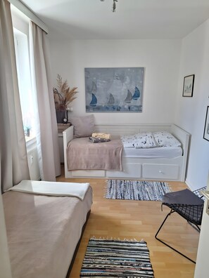 Un dormitorio con cama, una mesita de noche con lámpara, un cuadro en la pared y una ventana con cortinas.