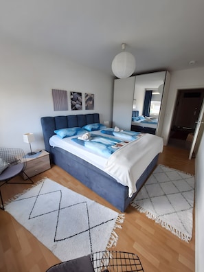 Ein modernes Schlafzimmer mit einem Bett, Nachttischen, einem Sessel und einem großen Spiegel.