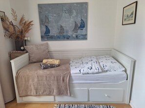 A bedroom with a bed, a bedside table with a clock, a potted plant, and a wall painting. - Bright Holiday Apartment with Balcony Near the Beach (Lübeck)
