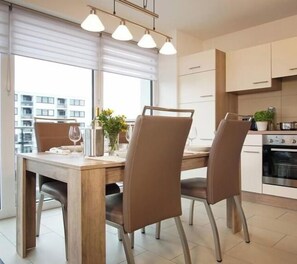 A modern kitchen with a dining area, featuring a wooden table, four chairs, and pendant lighting. - Holiday apartment with 2 bedrooms (Heiligenhafen)