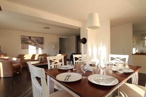 Een eetgedeelte met een houten tafel gedekt voor vier personen, witte stoelen en een moderne hanglamp.