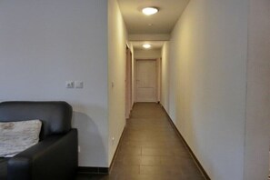 A narrow hallway with a door at the end, a black sofa with a cushion, and a light fixture on the ceiling. - Holiday apartment W17.2 (Graal-Müritz)