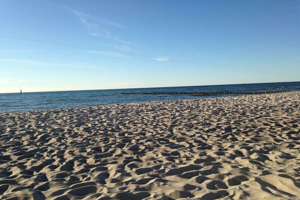 Une plage de sable fin, un ciel dégagé et une jetée en bois qui s’avance dans l’eau.
