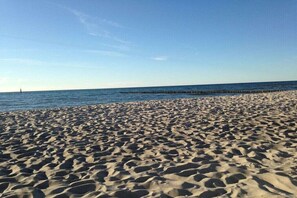 Een zandstrand met een heldere lucht en een houten steiger die het water in reikt.