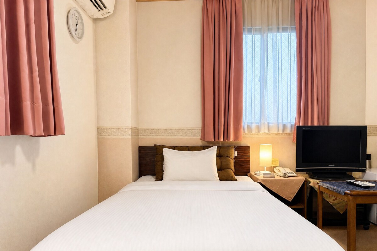 A hotel room with a bed, a bedside table with a lamp, a telephone, and a television.