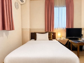 A hotel room with a bed, a bedside table with a lamp, a telephone, and a television.