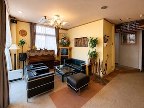 A hotel room with a sofa, armchair, ottoman, television, and a painting on the wall. - WASHUKAN HOTEL  (Gyoda)