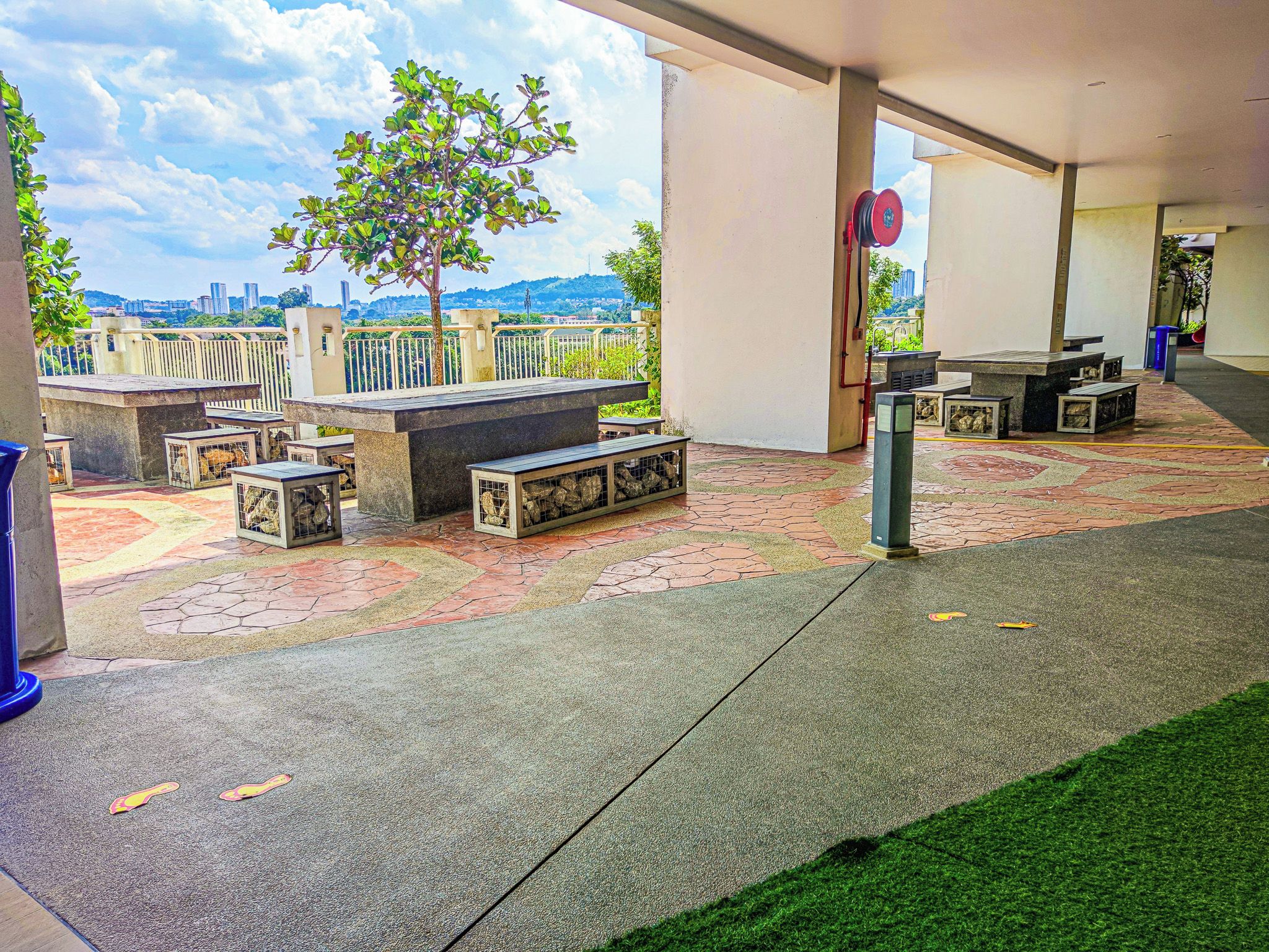 An outdoor seating area with tables and benches, a tree, and a view of a cityscape.