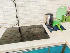 Une cuisine avec une plaque de cuisson à induction noire, une bouilloire verte et une planche à découper verte posée sur le plan de travail.
