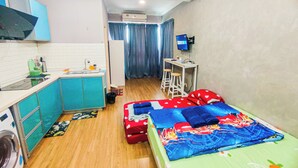 A compact room with a kitchenette, a bed with a colorful bedspread, a desk with a computer, and a washing machine. - Cozy Suites at Saville Cheras by HCK (Cheras)
