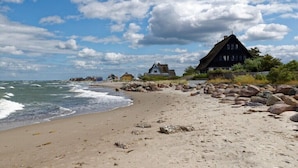 Une plage avec une maison au toit de chaume, un rivage rocheux et un ciel dégagé.