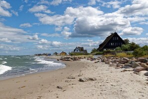 A beach with a thatched-roof house, a rocky shoreline, and a clear sky. - Holiday apartment with 3 bedrooms (Heiligenhafen)