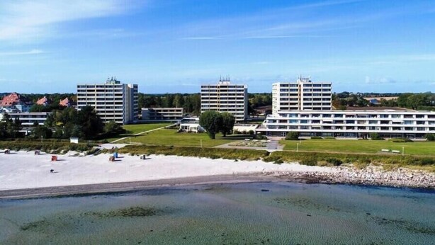 Ett hotell vid kusten med flera byggnader, en sandstrand och en klar himmel.
