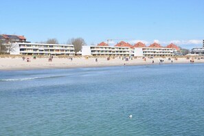 Ein Küstenhotel mit mehreren Balkonen, einem Sandstrand und einem ruhigen Meer.