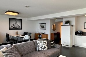 A modern living room with a sofa, a dining area with a table and chairs, and a kitchen area with cabinets and appliances. - House Zur Mole, Apartment 13 "Sea View" (Großenbrode)