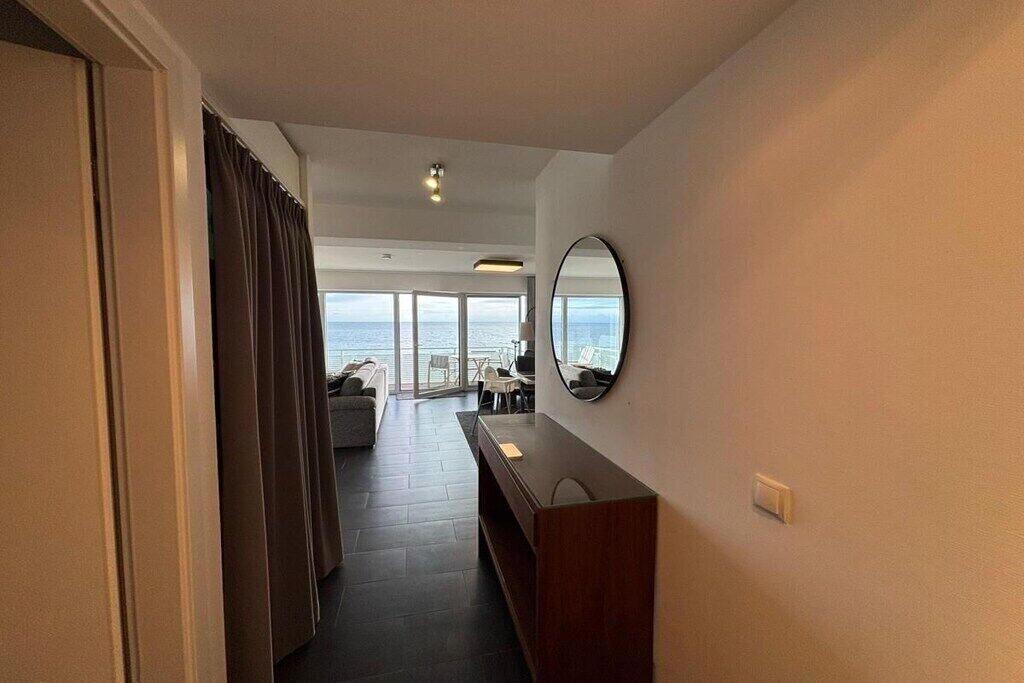 Een hotelkamer met uitzicht op zee, een houten console, een spiegel en een schuifdeur naar een balkon.