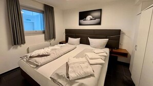 Una habitación de hotel con una cama grande, una mesita de noche, una ventana con cortinas y un cuadro colgado en la pared.