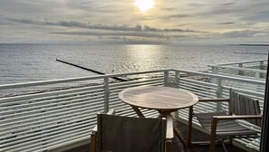 Terraza de madera con una mesa redonda y sillas con vista a un cuerpo de agua.