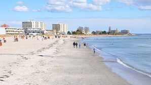 Una playa con edificios al fondo, una orilla arenosa y gente caminando.