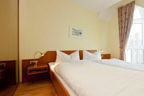 A hotel room with a large bed, a bedside table with a lamp, a wall-mounted artwork, and a window with curtains. - Holiday apartment in Norderney with Wi-Fi (Norderney)