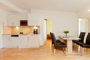 Una cocina moderna con armarios blancos, horno empotrado y comedor con mesa de madera y sillas negras.