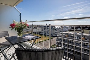 Un balcon agrémenté de meubles en osier, une table avec un magazine et un vase rempli de fleurs.