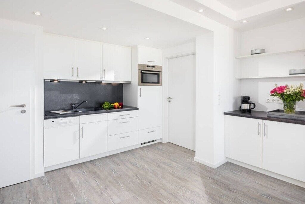 Una cucina moderna con mobili bianchi, un piano di lavoro nero e un forno in acciaio inossidabile.