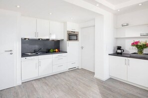 Une cuisine moderne avec des meubles blancs, un plan de travail noir et un four en acier inoxydable.