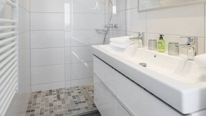 Et moderne badeværelse med en stor hvid vask, bruser og flisegulv.