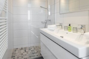 Un baño moderno con un lavamanos grande de color blanco, una ducha y suelo de baldosas.